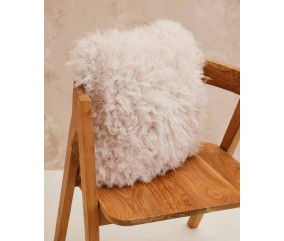 Coussin Maeve tricoté en fausse fourrure écru à longs poils, posé sur un fauteuil en bois - Patron tricot Phildar