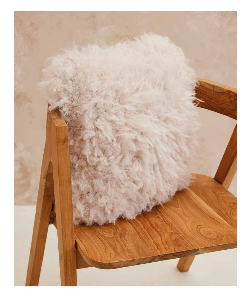 Coussin Maeve tricoté en fausse fourrure écru à longs poils, posé sur un fauteuil en bois - Patron tricot Phildar
