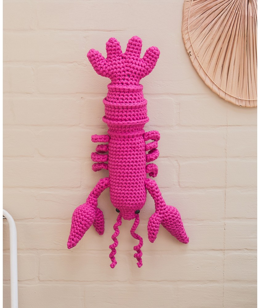Homard Salerne crocheté en rose vif, suspendu sur un mur clair, 40 cm de long - Patron crochet Pingouin