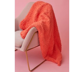 Plaid Dada corail en grosses mailles, drapé sur un fauteuil doré devant un fond rose - Patron Pingouin