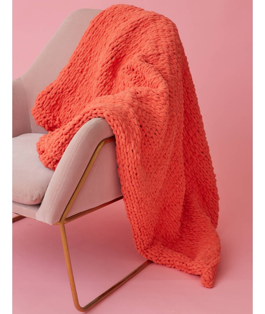 Plaid Dada corail en grosses mailles, drapé sur un fauteuil doré devant un fond rose - Patron Pingouin