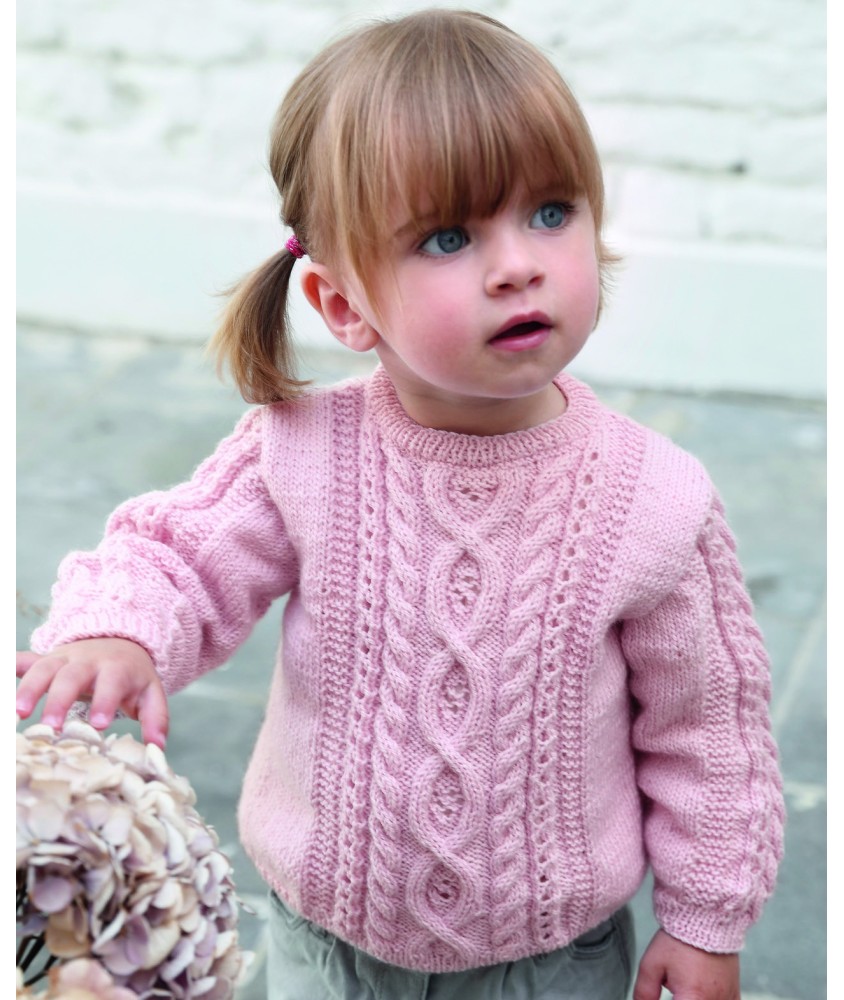 Pull Isalys rose à torsades et motifs de cœurs en relief, porté par une petite fille - Patron tricot Phildar
